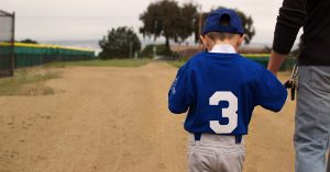 A boy dressed in a blue baseball uniform walking with his dad