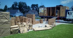 Large amount of boxes piled in a driveway with a large moving truck in the background